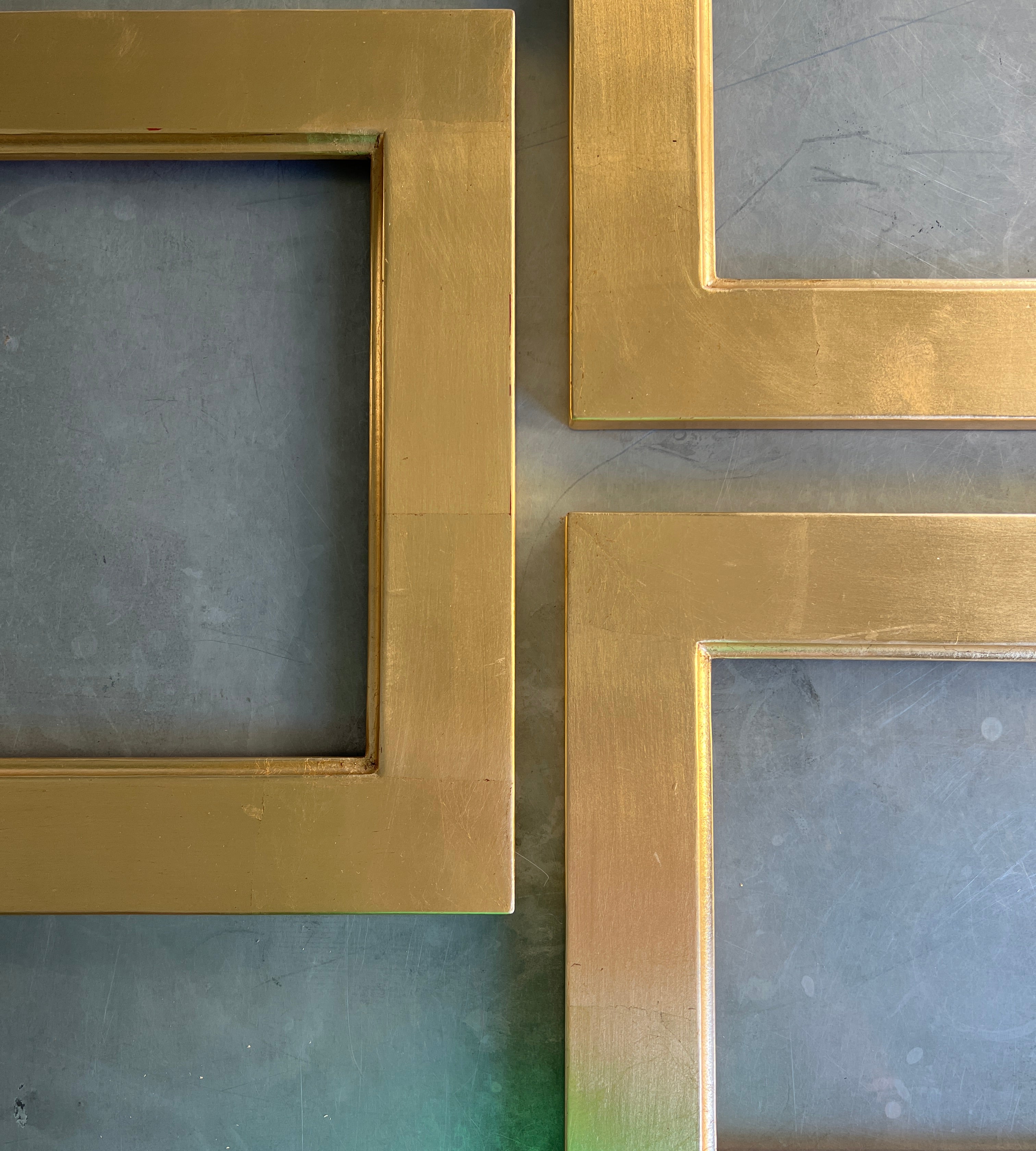 Three empty square picture frames with brushed gold metal borders arranged on a textured dark gray wall.